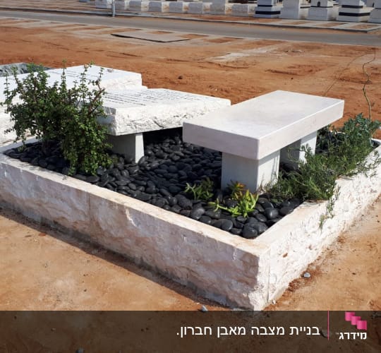 מצבה מיוחדת מאבן טבעית בשילוב חלוקי נחל שחורים, צמחייה וספסל אבן